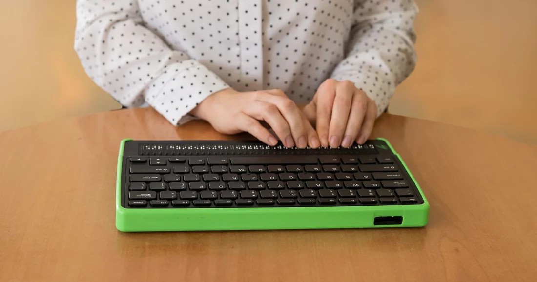 A woman typing on a braille keyboard for computer with a green frame