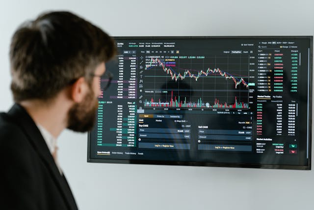 A man intently gazes at a stock market monitor, analyzing trends and data with a focused expression.