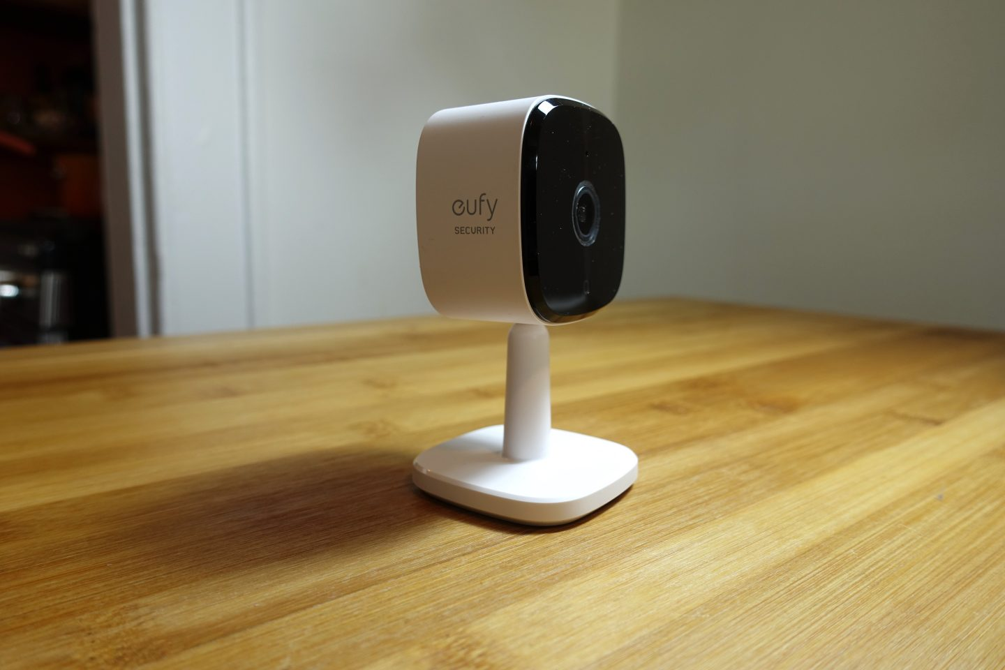 How to Reset Eufy Indoor Camera: white Eufy indoor security camera standing on a wooden surface, facing forward with its black lens panel visible. The sleek design blends into the background, highlighting its compact yet functional form."