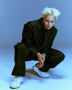 This contain. Mino sitting on the ground with his hands in his pockets and wearing white sneakers