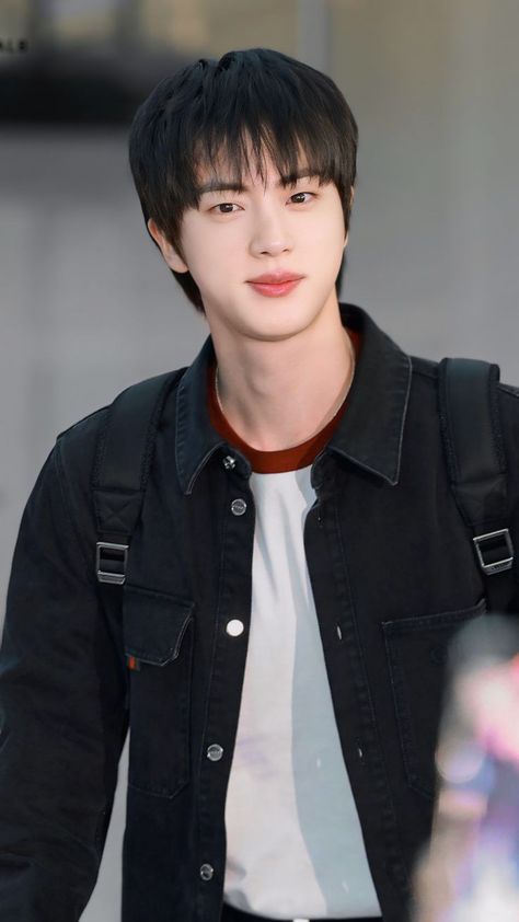 This contain Jin with black hair wearing a jacket and white t - shirt is looking at the camera