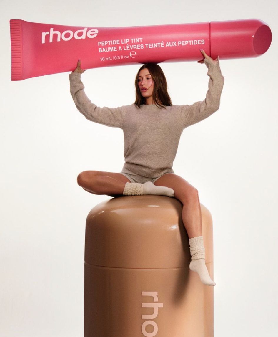 A person sitting on a large tube of cream

Description automatically generated