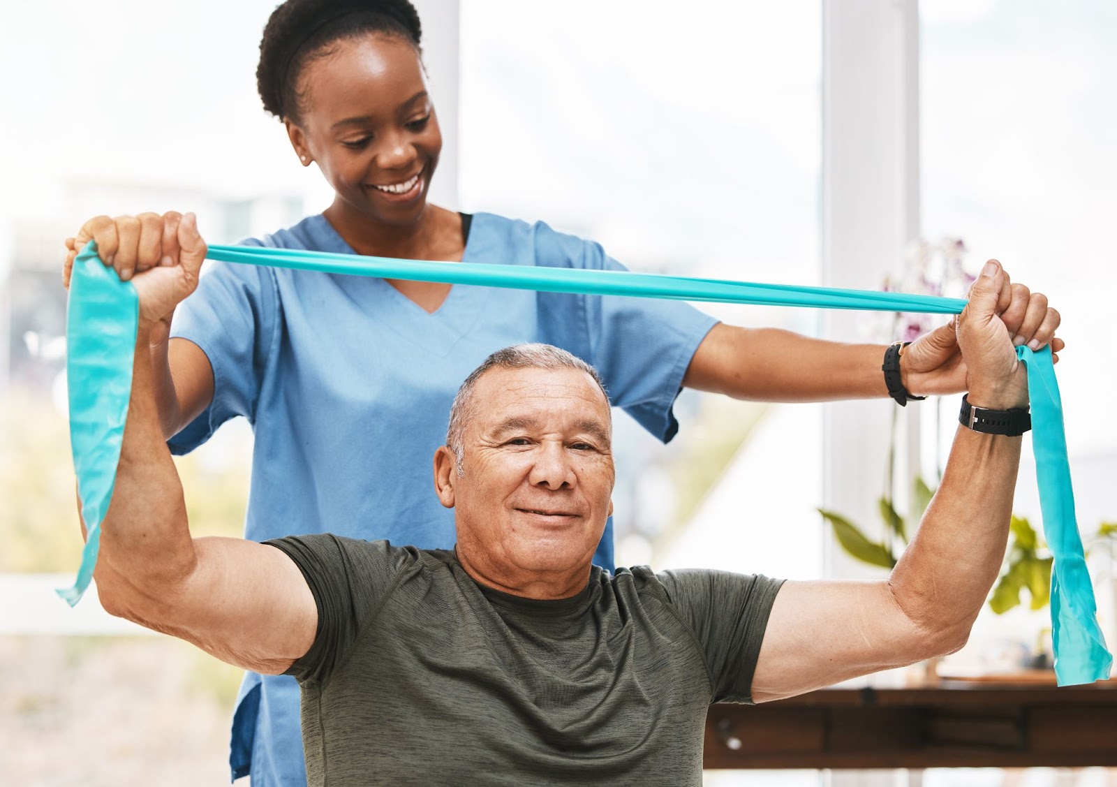 A personal care home staff member helps a male resident use a resistance band to perform physical therapy exercises.