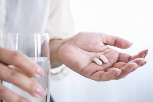 A woman holding a glass of water in one hand and a supplement capsule in the other for supporting gut health and bloating.