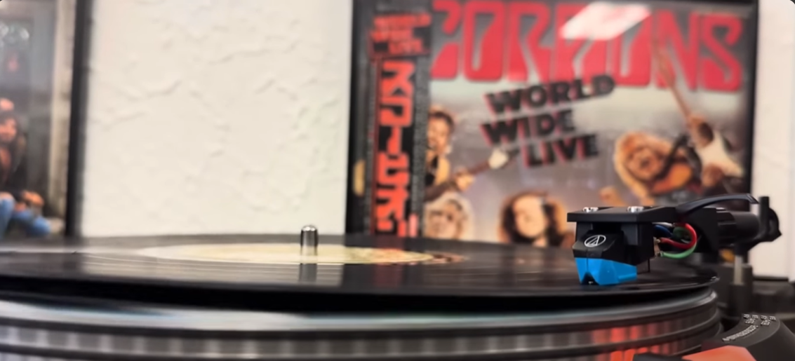 A turntable playing a vinyl record with the album cover of Scorpions' 'World Wide Live' in the background.