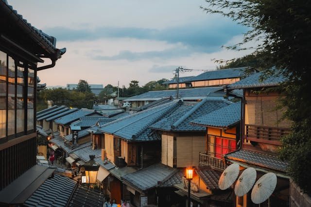 A scenic view of a traditional Japanese village showcases architectural conservation with wooden houses under a cloudy sky. The rooftops, mostly tiled, highlight cultural heritage as the street, lined with glowing lanterns, reflects community engagement.