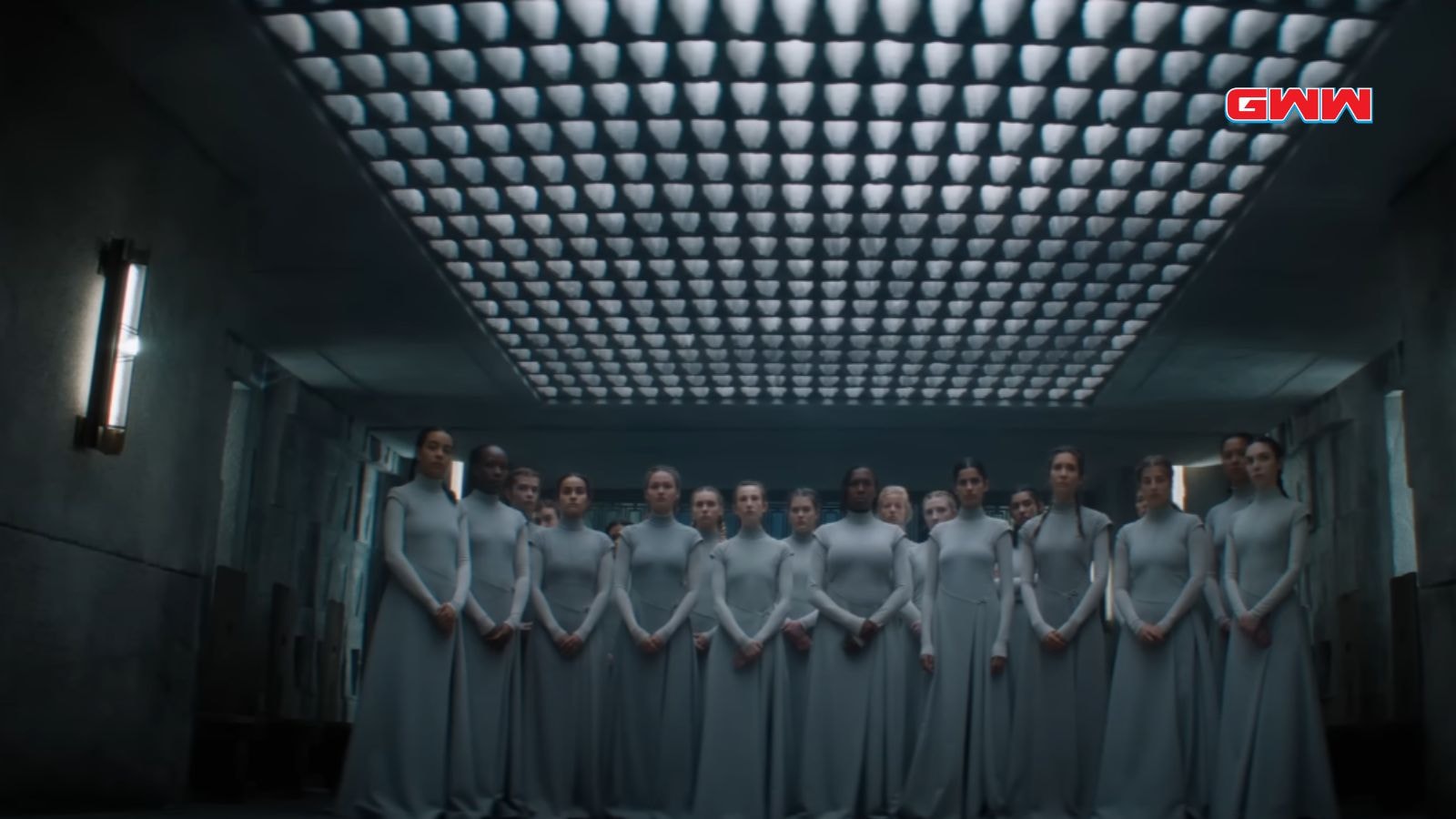 Group of Bene Gesserit in grey dresses standing in formation under patterned ceiling.