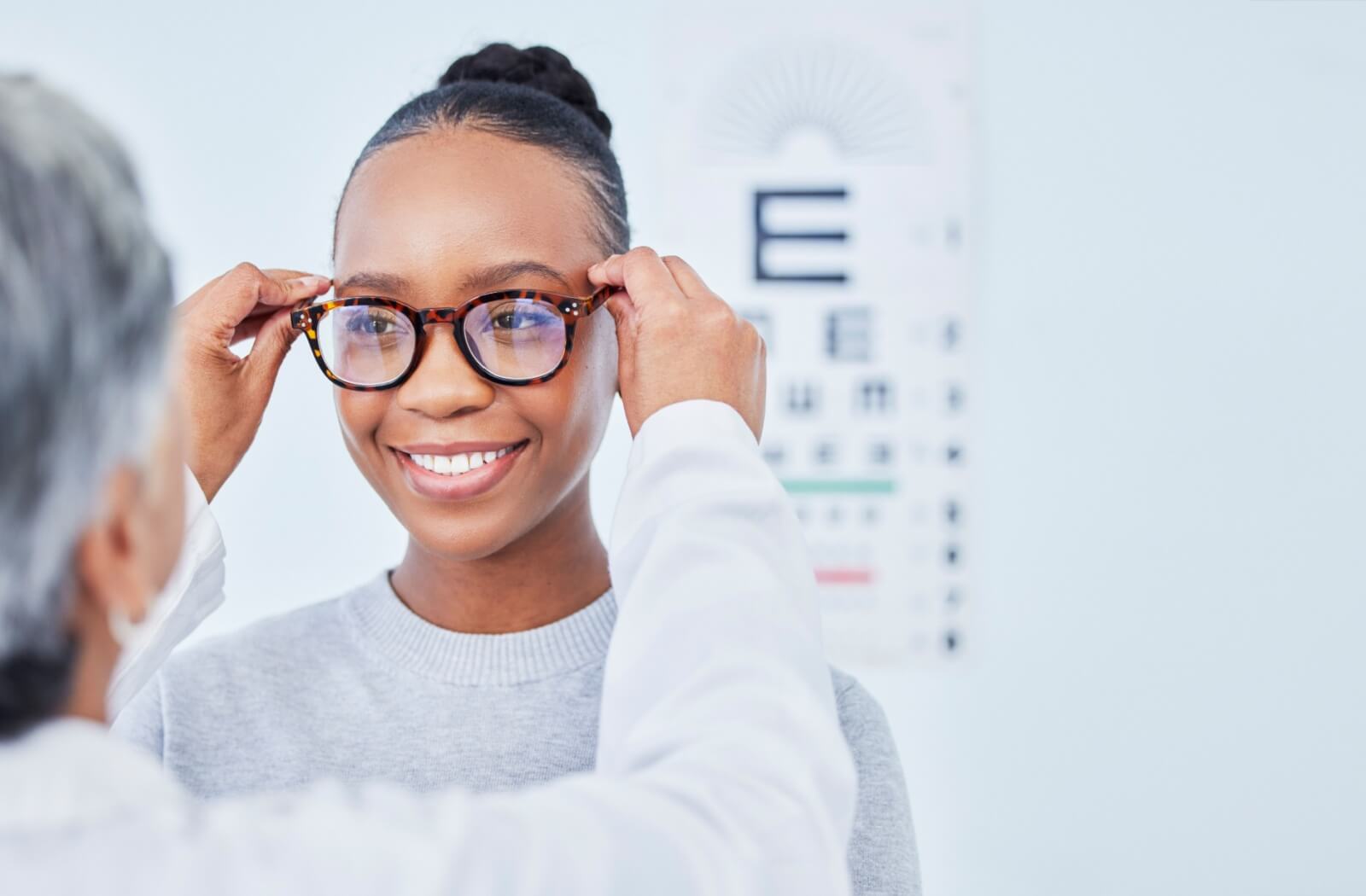 An optometrist helps their patient try on a new pair of glasses after an eye exam.
