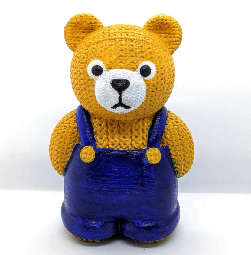 Knitted-style 3D printed bear figure with yellow yarn texture, white snout, and blue overalls, designed by Anukalpgenesis3d


