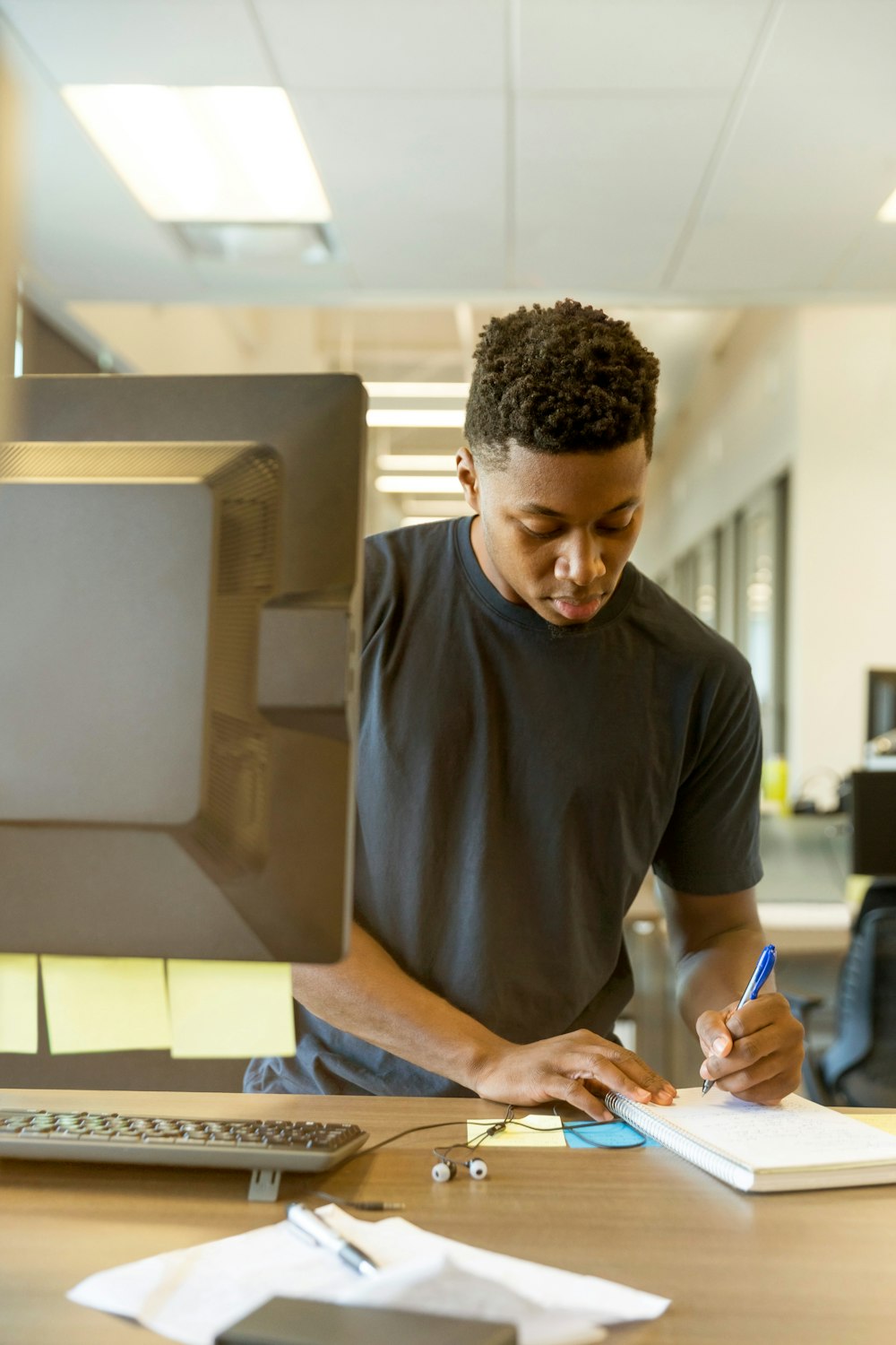 A young black man leans over a desk and writes on paper - Earn Free Money for College with the Oregon Promise Grant!