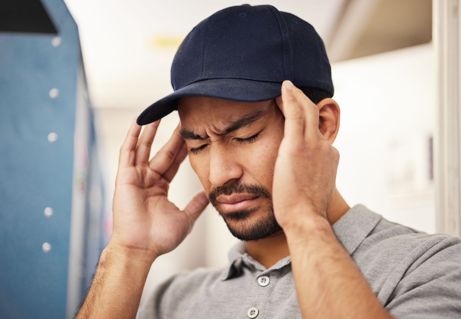 A man wearing a hat and holding his hands to his head with an uncomfortable facial expression. 