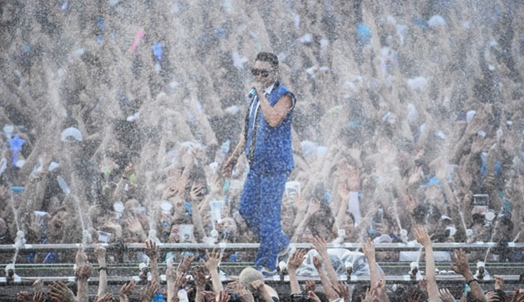 A person in blue suit and sunglasses standing in front of a crowd of peopleAI-generated content may be incorrect.