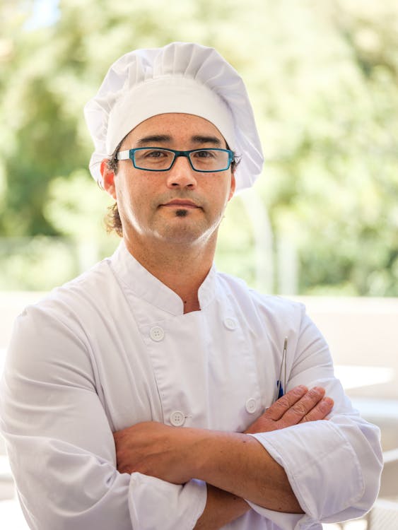 Free Professional male chef wearing glasses and toque blanche, standing confidently with crossed arms. Stock Photo