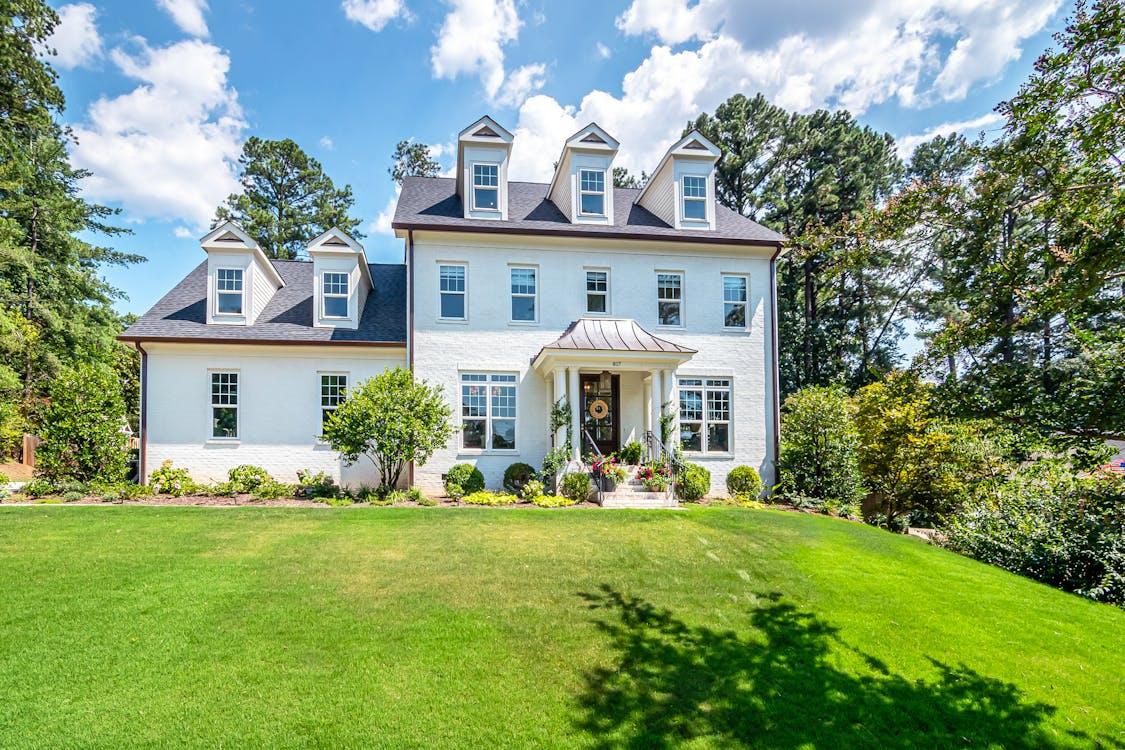 Free Beautiful colonial-style house with a lush green lawn and blue sky, perfect summer property. Stock Photo