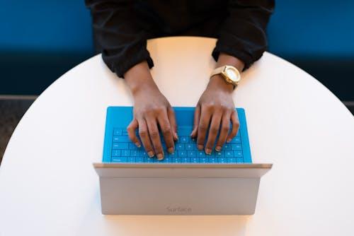 Free Hands of a person typing on a laptop with a blue keyboard, taken from above, ideal for technology themes. Stock Photo