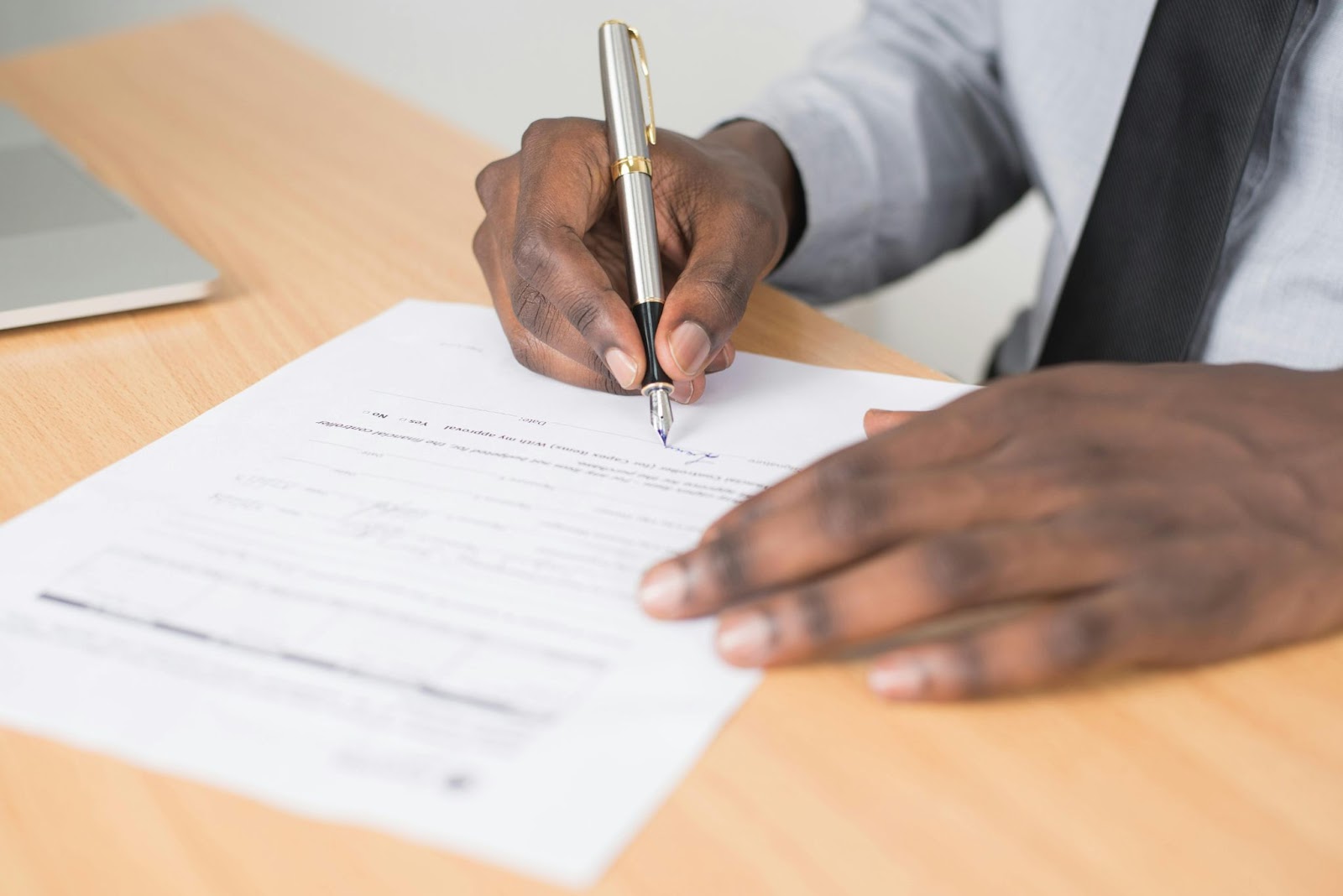 A person signing a document with a pen on a wooden desk.