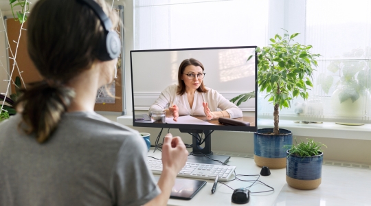 Femme avec des écouteurs en appel vidéo avec une nutritionniste sur un ordinateur dans un bureau à domicile.