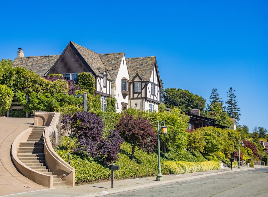 Free Beautiful Tudor style house with lush greenery on a sunny day, perfect for real estate listings. Stock Photo