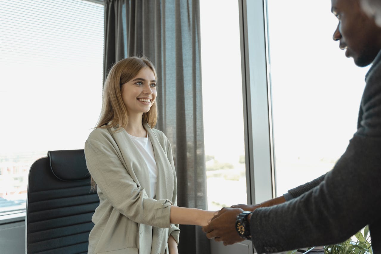 A man and woman shake hands in a modern office setting, symbolizing a successful business agreement or collaboration.