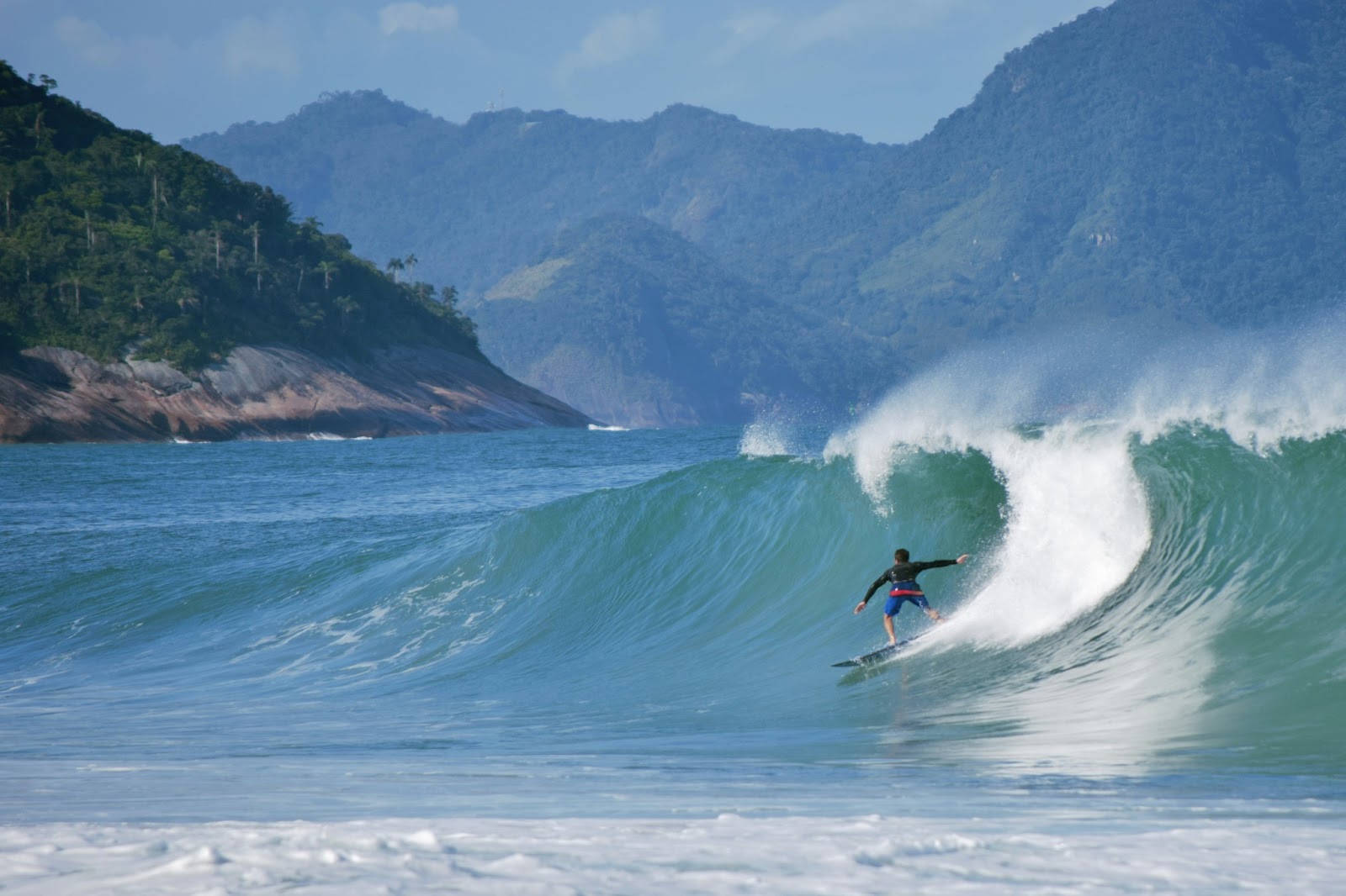 Beautiful day at Praia da Pipa beach, featuring surfers catching waves and golden hues over the ocean.