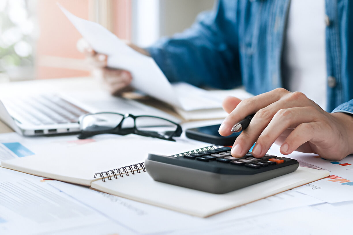 Person using a calculator while reviewing financial documents, representing the process of financial forecasting and strategic planning.