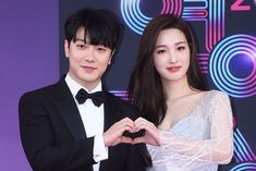 This contains a picture of Yulhee and FTISLAND's Choi Minhwan standing next to each other in front of a purple wall with the word love written on it