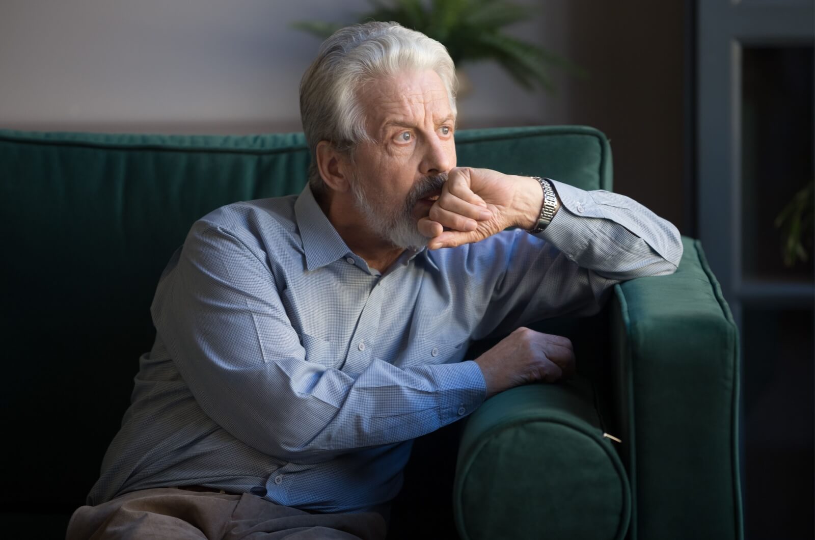 An older adult experiencing loneliness sitting on a couch and looking out the window.
