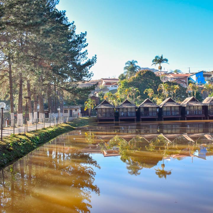 Uma visualização relaxante de cabanas ao lado de um lago refletindo a natureza ao redor em um dia ensolarado. Ótimo destino para turistas que buscam tranquilidade e beleza natural.
