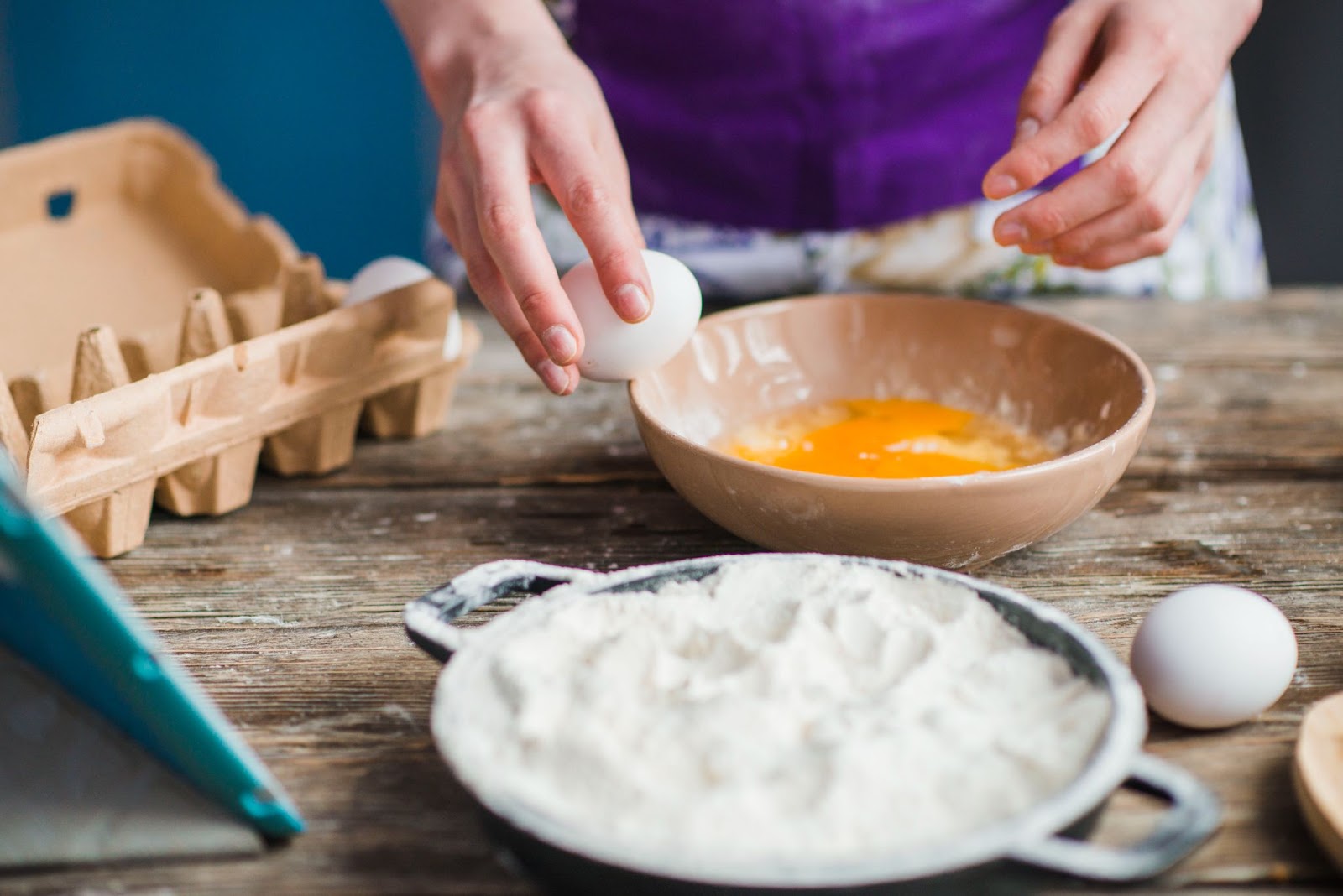 on a table top Eggs being cracked into a bowl with a separate bowl of flour nearby.