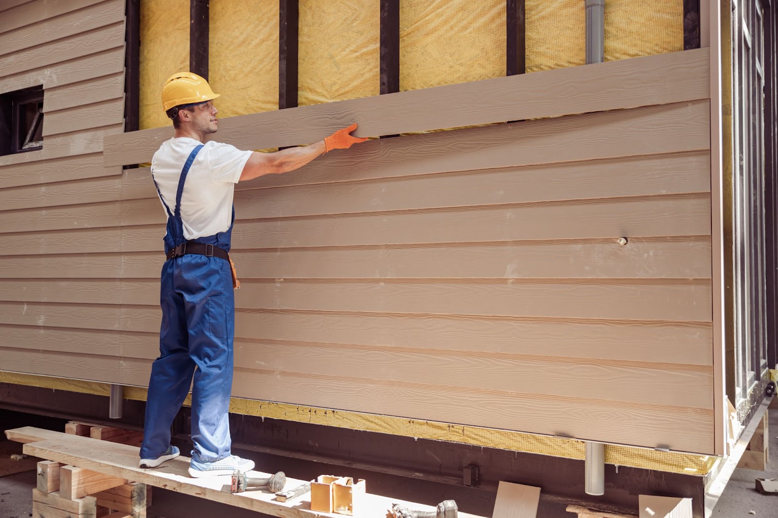 A construction worker installs sidings outside the house.