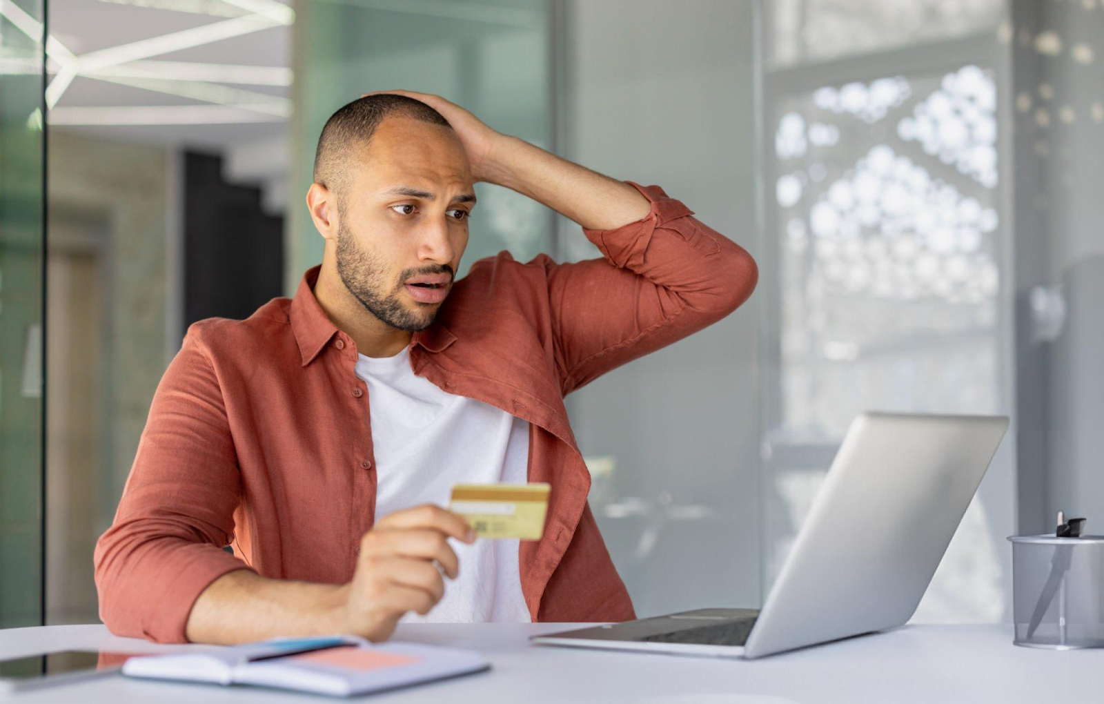 A man worriedly looking at coputer screen with a credit  card in his hand