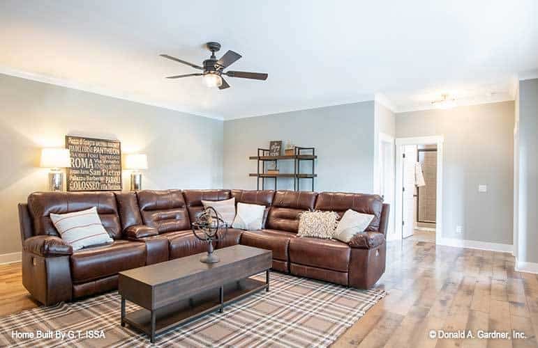 Recreation room with an L-shaped leather sectional and a wooden coffee table over a plaid area rug.