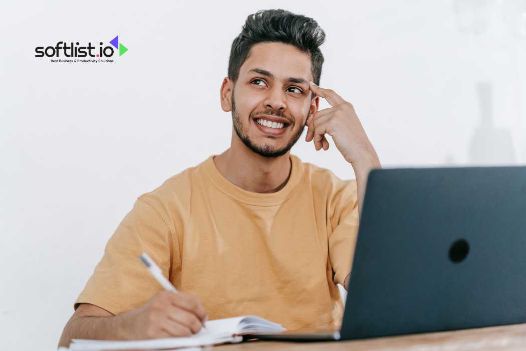 Smiling man writing notes with a laptop in front of him