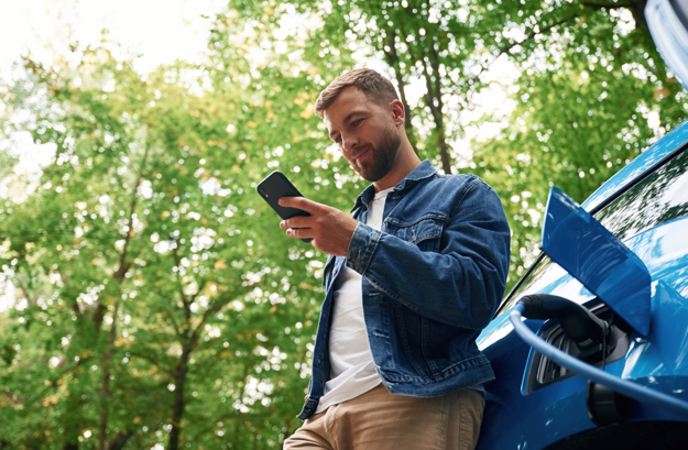  Hombre revisando su dispositivo móvil mientras espera que se cargue su auto eléctrico.  