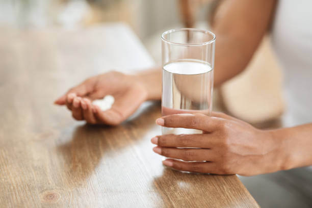 A close-up of a person holding a magnesium L-threonate capsule in one hand and a glass of water in the other, ready to take the supplement for better brain health.