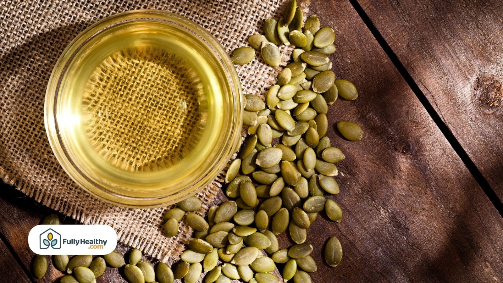 Glass bowl of pumpkin seed oil with raw seeds on burlap surface