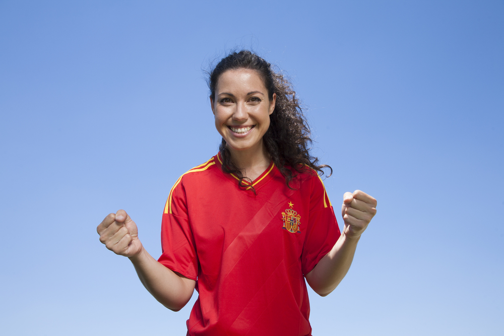 A joyful woman celebrating in a red Spain national soccer jersey.