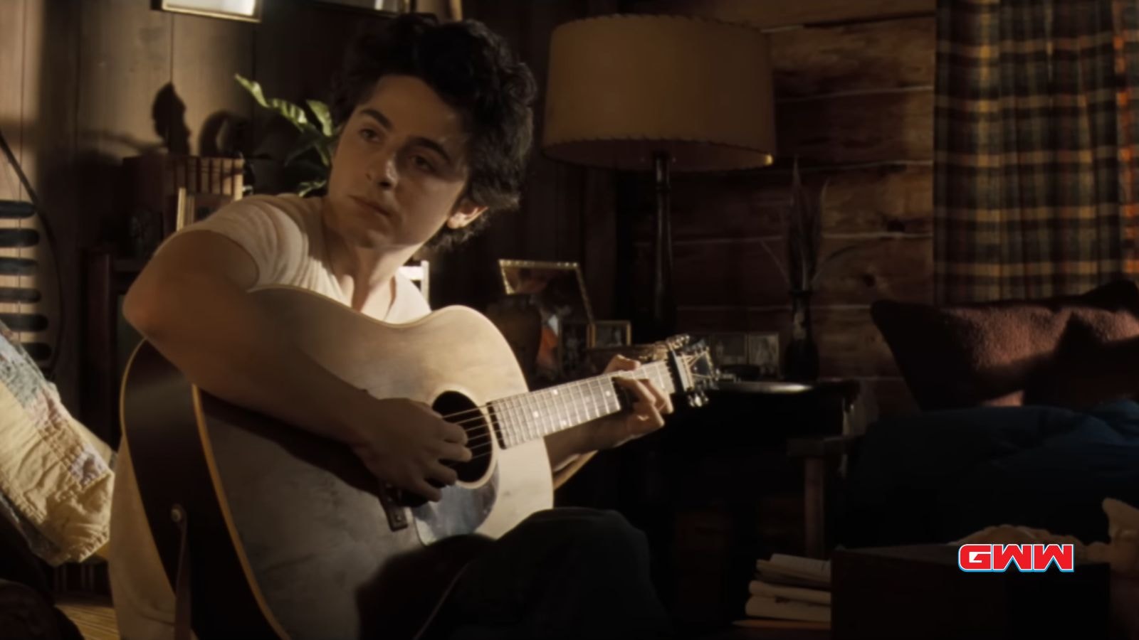 Bob Dylan plays guitar in a cozy, dimly lit cabin.