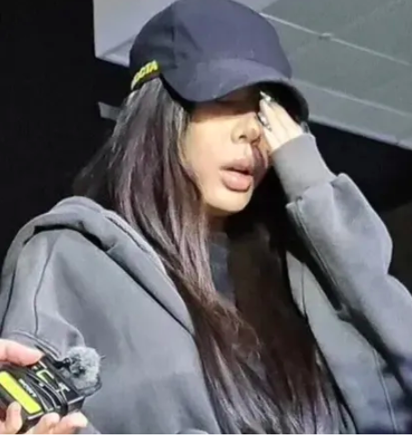 This contains an image of Jessi wearing a black hoodie and a black cap with her hand on her face