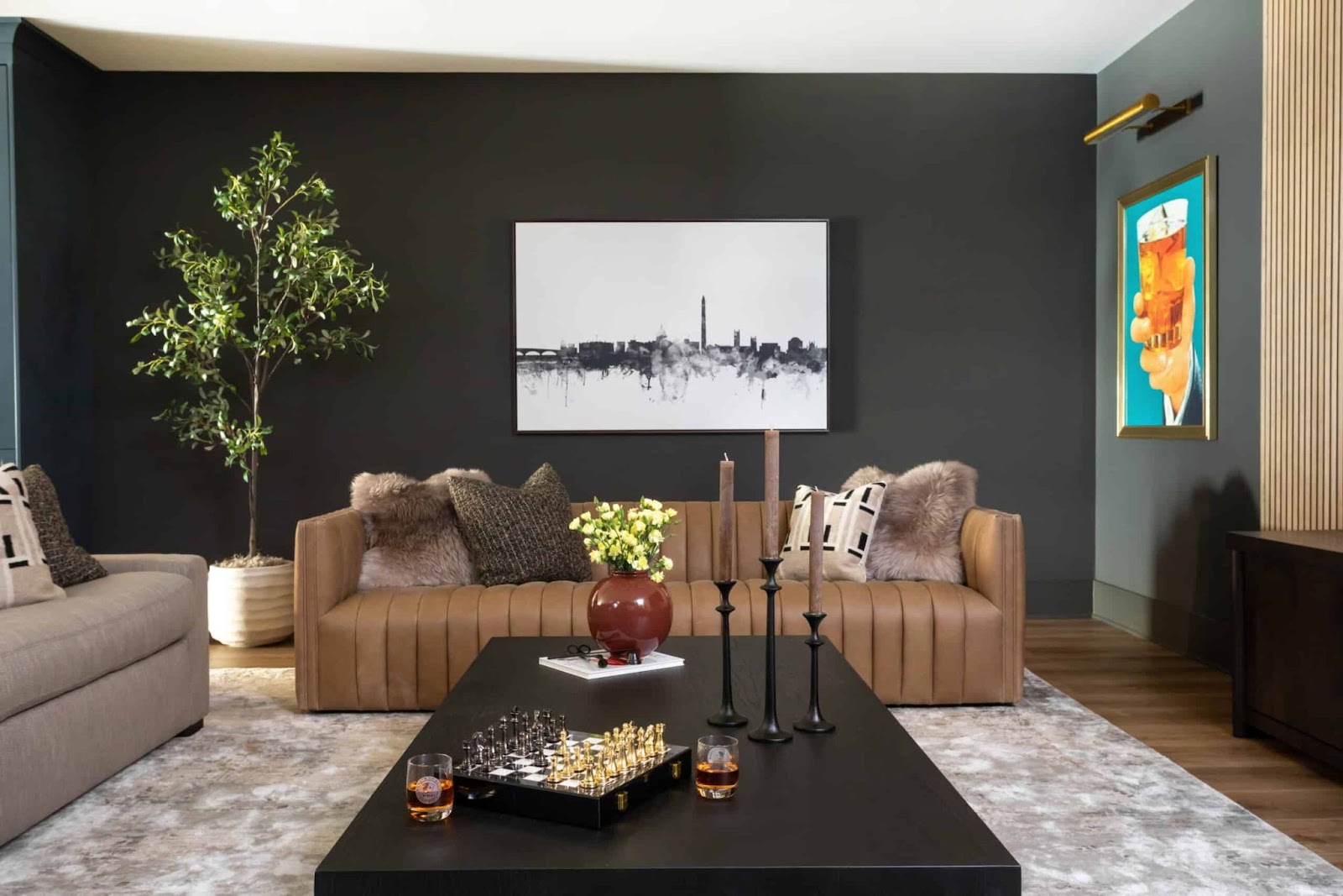 Living room setting with brown leather couch, black coffee table, chess board, and city art. 