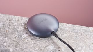 Bagian belakang Anker Wireless Charging Pad, yang diletakkan pada permukaan bermotif batu abu-abu, dengan latar belakang merah muda muda.