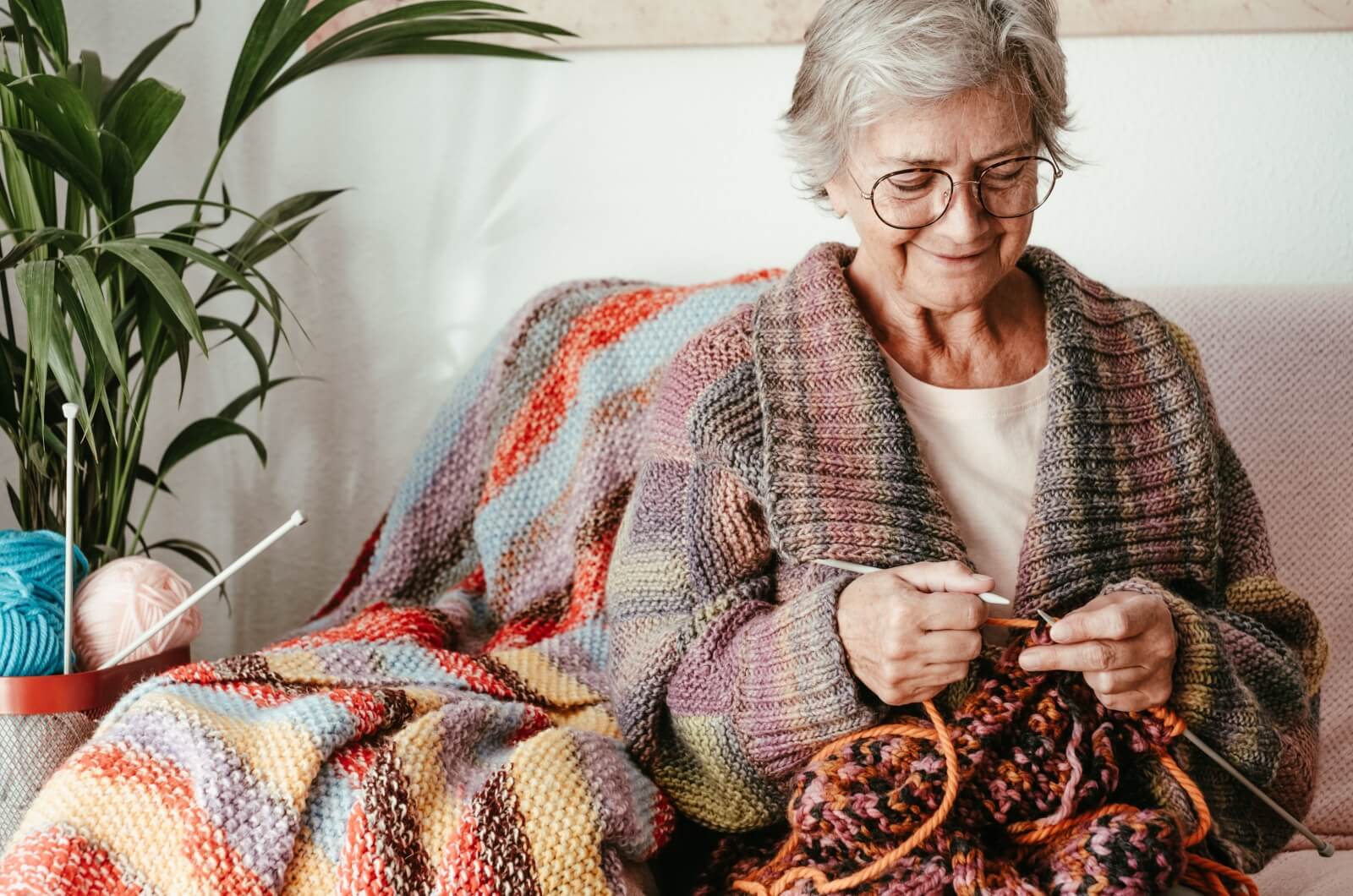  smiling older adult sitting on the couch and knitting.