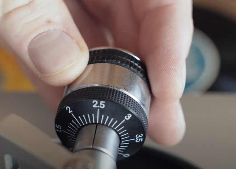 A person adjusting the tonearm counterweight on a turntable to set the tracking force.







