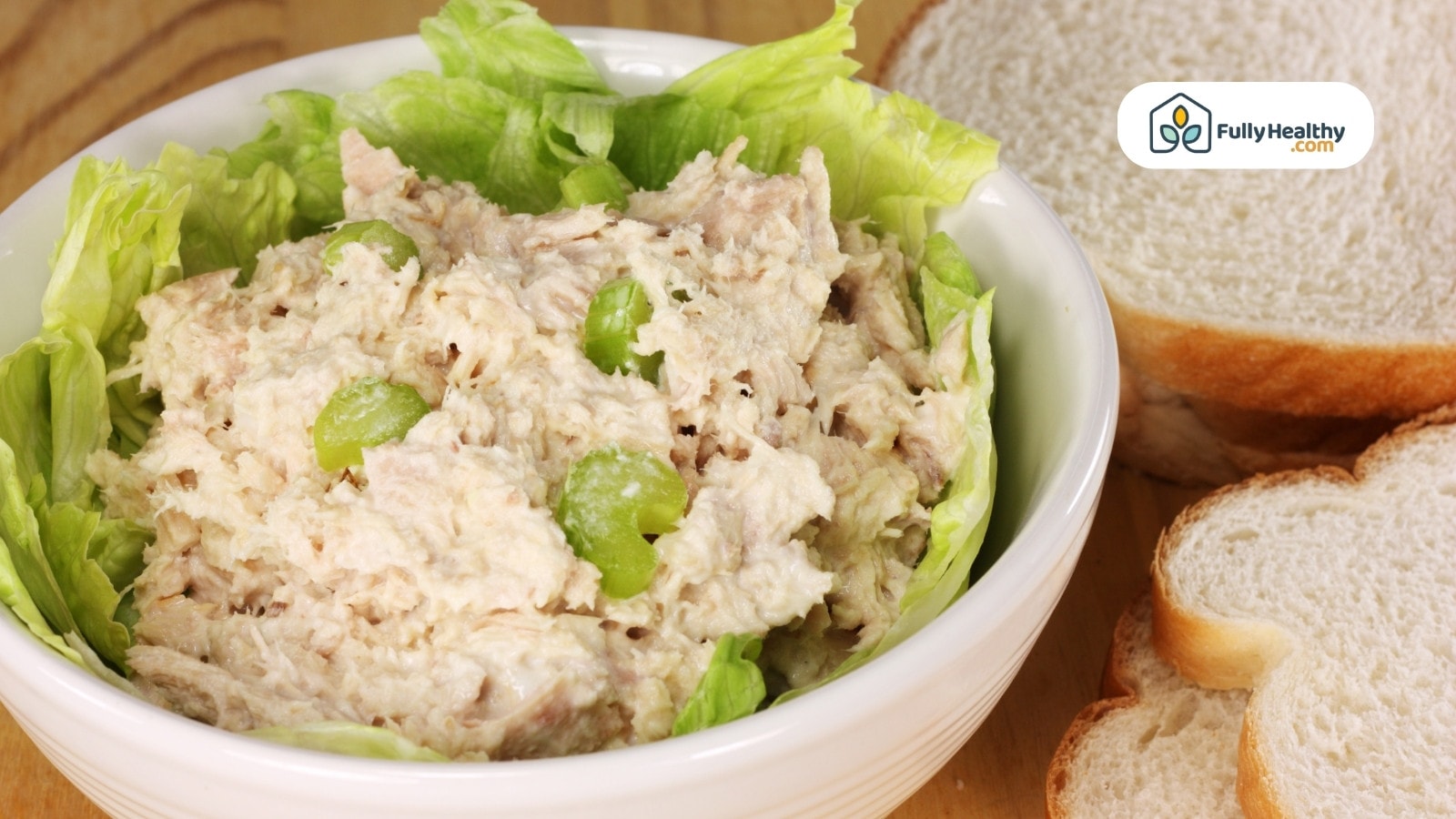 A bowl of tuna salad served with slices of bread on the side