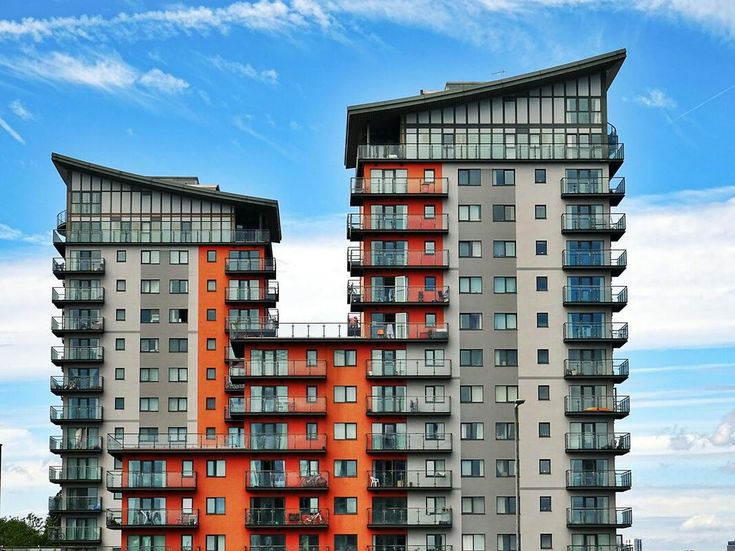 Foto dua gedung kondominium modern dengan desain arsitektur unik dan balkon kaca, berdiri di bawah langit biru cerah, mencerminkan gaya hidup urban yang eksklusif.