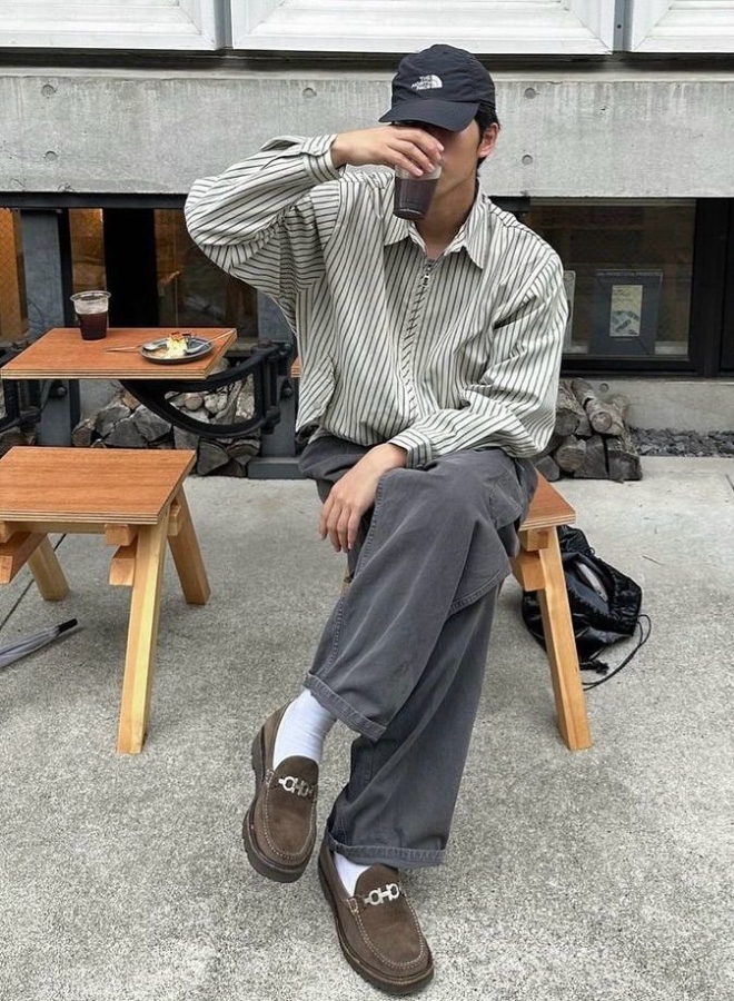 Pria mengenakan kemeja oversized, jeans abu-abu, dan loafers.