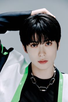 A picture of NCT Jaehyun wearing a black jacket mixed with white, green and a black inner shirt with his hand on his head