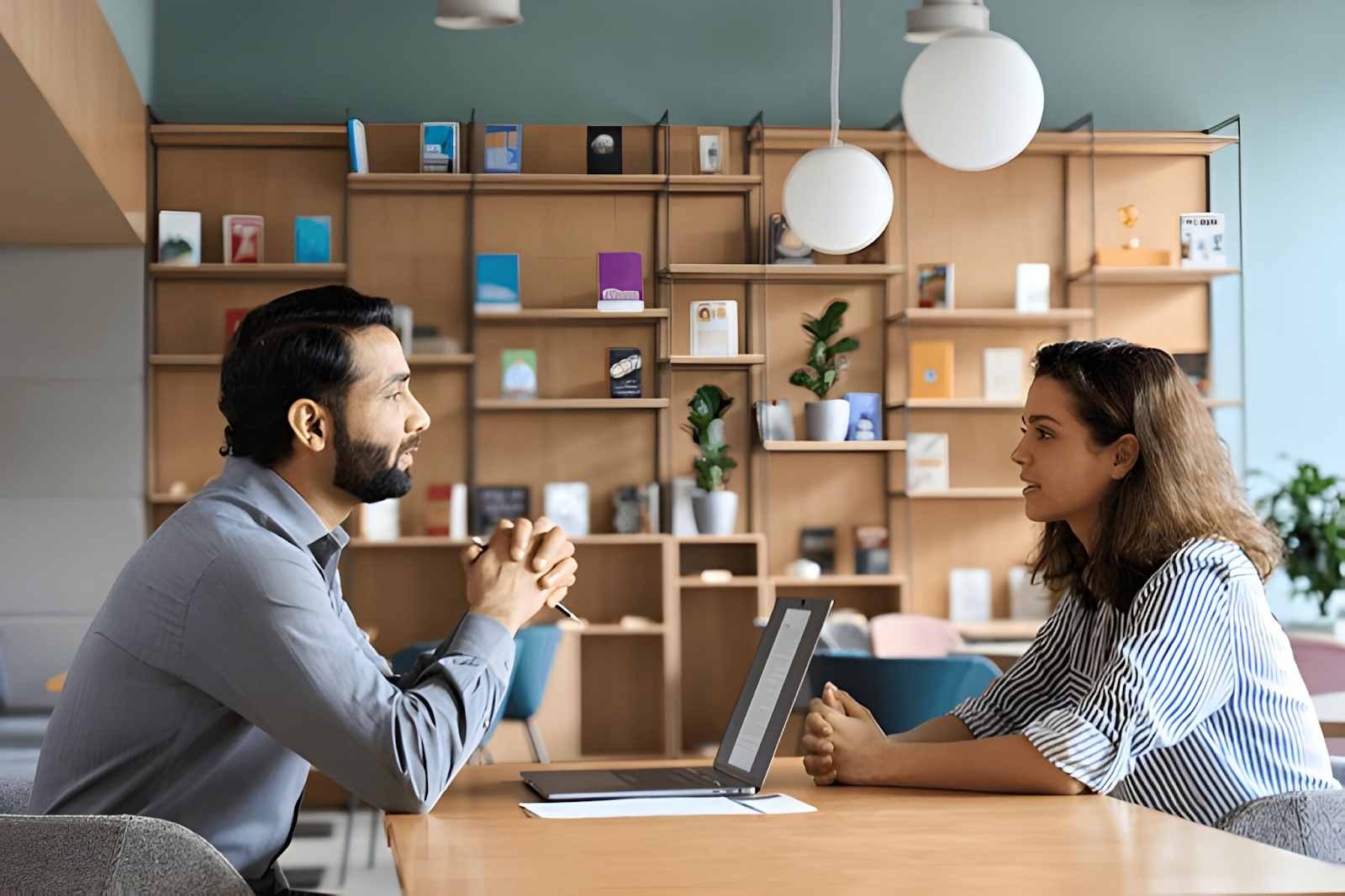 Two people having a discussion at a table, highlighting the importance of hiring employees when needed for a bookkeeping business.