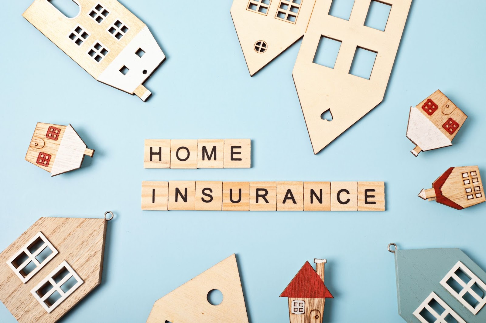 Words “home insurance” written using wood tiles next to wooden models of homes. 