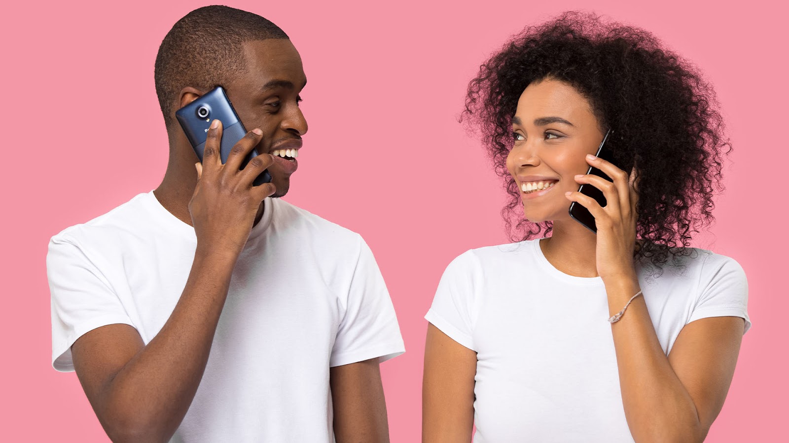 Brunette man and woman wearing white shirts looking and smiling at each other holding phones to their ears